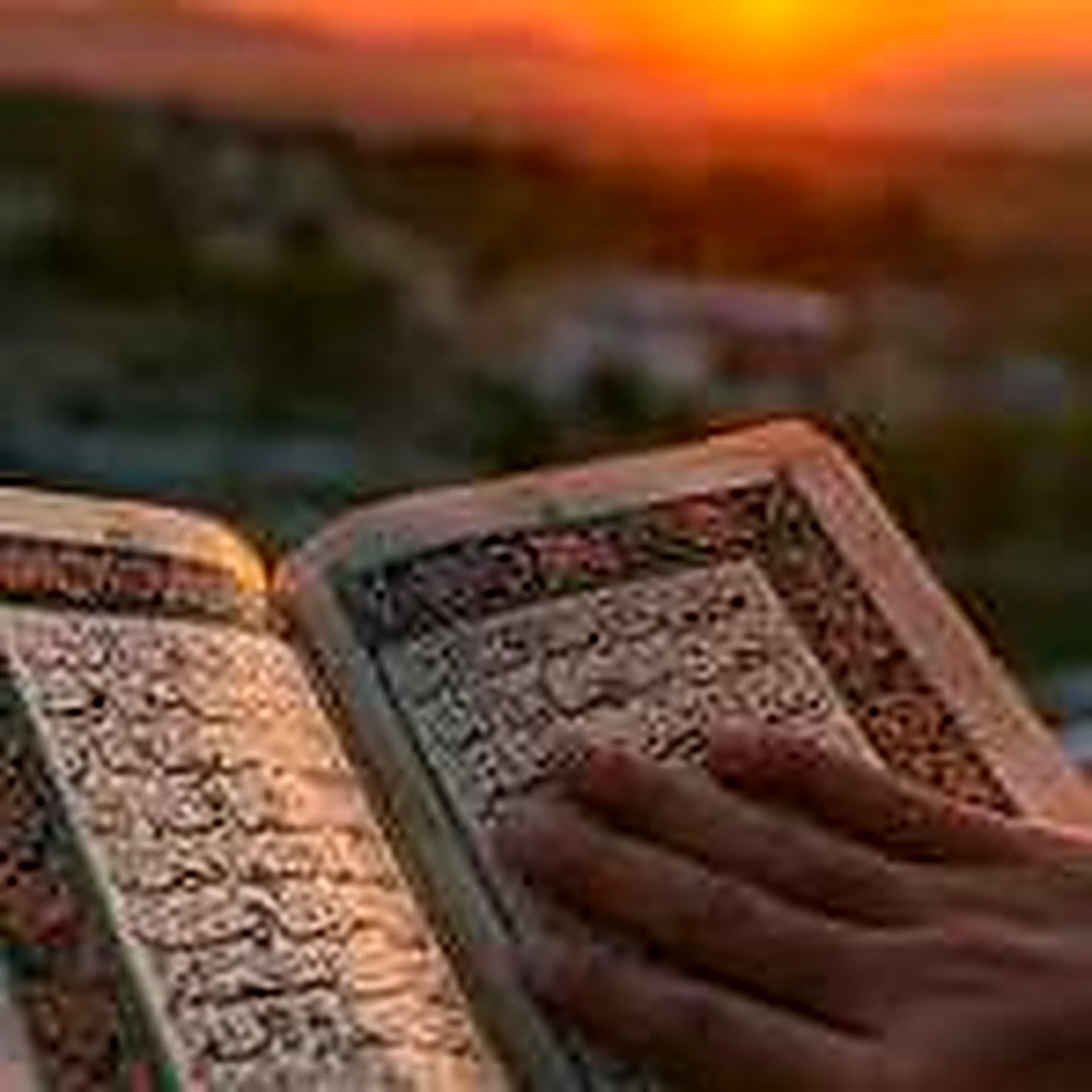 Hands resting on an open Quran at sunset
